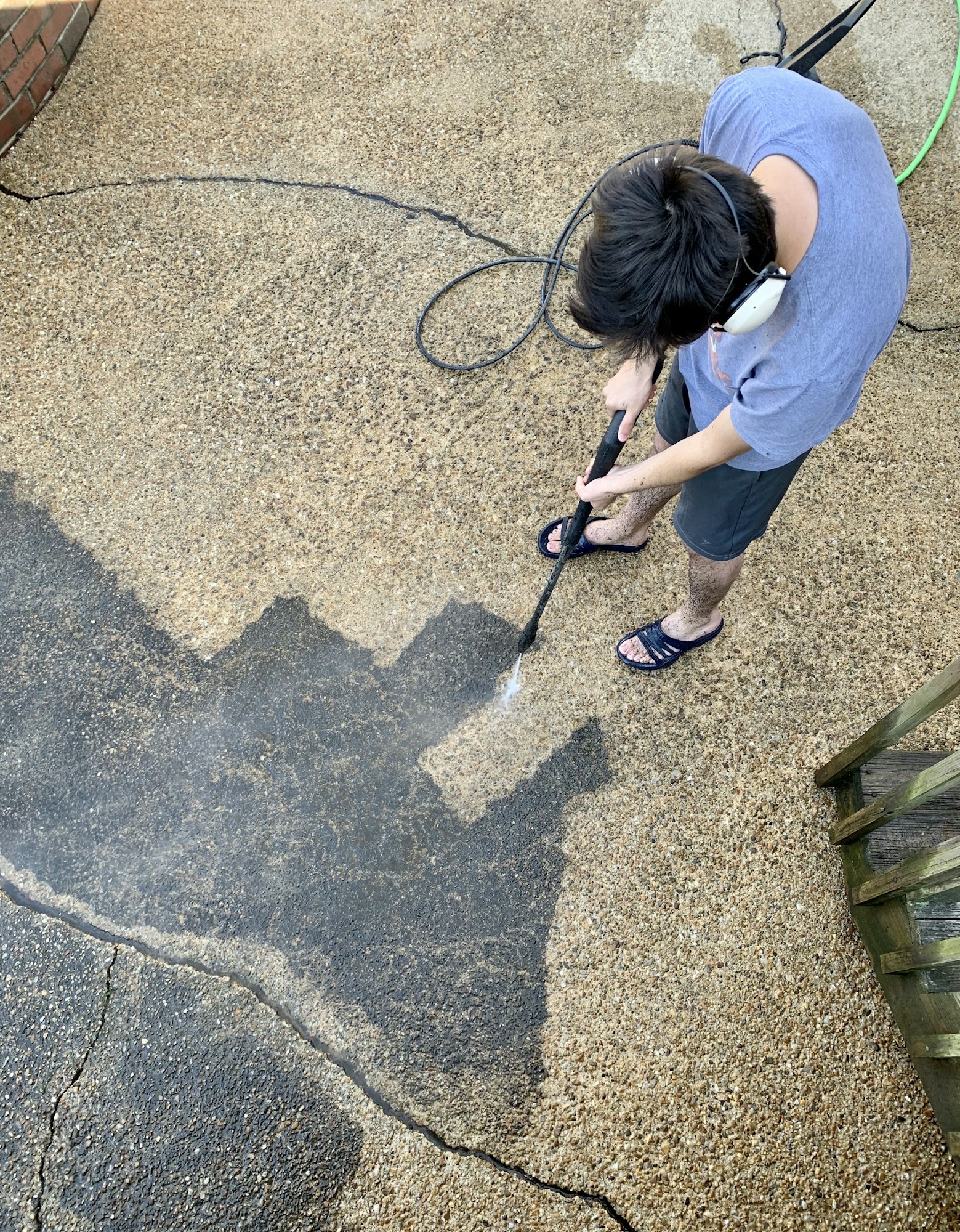 Overhead of a young GenZ adult man doing house chores power washing the patio